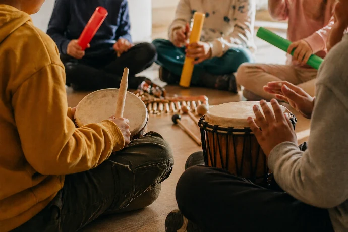 Laboratorio musicale di gruppo per bambini e ragazzi seduti in cerchio con djembe, tamburi e tubi sonori colorati