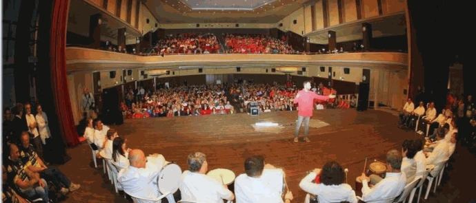 Orchestra inclusiva in semicerchio sul palco di un teatro gremito, durante un'esibizione pubblica